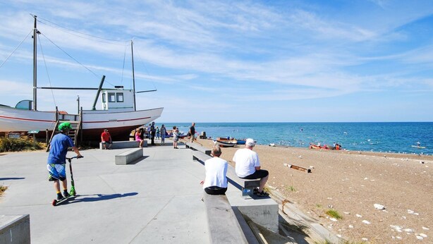 A pier with a boat docked, people walking, and a beach in the background.