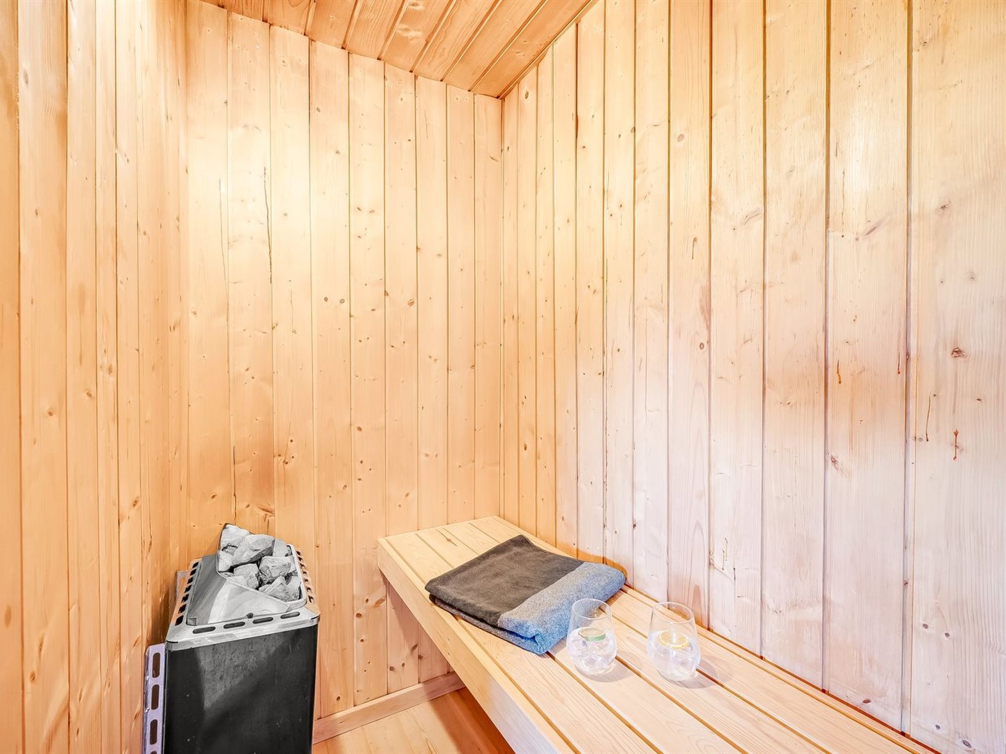 Un sauna aux murs en bois, un banc, une serviette et deux verres d’eau.