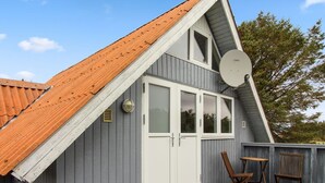 Kaksikerroksinen talo, jossa on kalteva katto, satelliittiantenni ja pieni patio, jossa on tuoleja.