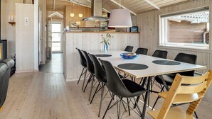 Uma sala de jantar espaçosa, com uma mesa grande, cadeiras pretas e uma poltrona de madeira. Uma luminária pendente moderna ilumina a mesa, e uma janela permite a entrada de luz natural.