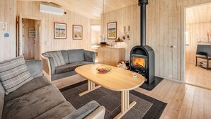 A cozy cabin interior with a sofa, a wooden table, and a wood-burning stove. - "Benjamina" - 530m to the fjord by Interhome (Tarm)