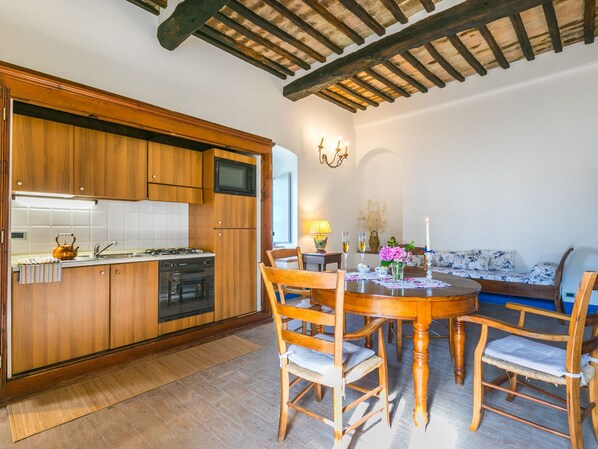 A kitchen with wooden cabinets, a microwave, and a stove. There is a dining table with chairs and a sofa in the living area.