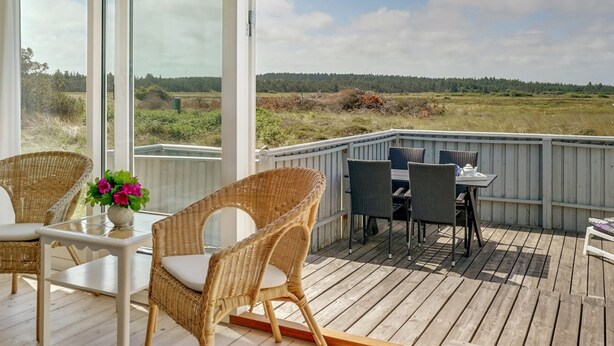 Une terrasse dotée de meubles en osier et d’une table, offrant une vue sur un paysage naturel.
