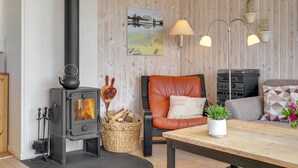 Un salon chaleureux avec un poêle à bois, un fauteuil en cuir, un canapé, une table à manger et un tableau accroché au mur.