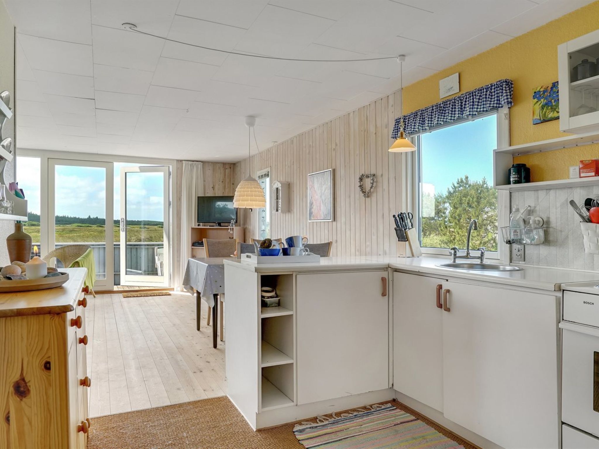 Une cuisine moderne avec des meubles blancs, une grande fenêtre et une vue sur l’extérieur.