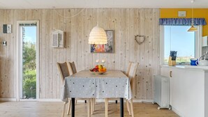 Un coin repas avec une table dressée pour quatre personnes, un luminaire suspendu et une vue sur l’extérieur par une fenêtre.