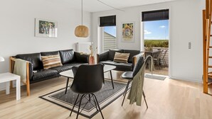 A modern living room with a black leather sofa, two black chairs, a white coffee table, and a hanging light fixture. There are two windows with blinds, a door leading outside, and artwork on the walls. - "Drita" - 2.3km from the sea by Interhome (Rømø)