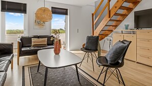 A modern living room with a sofa, two chairs, a coffee table, and a TV. There is a wooden staircase and a window with a view of the outdoors. - "Drita" - 2.3km from the sea by Interhome (Rømø)