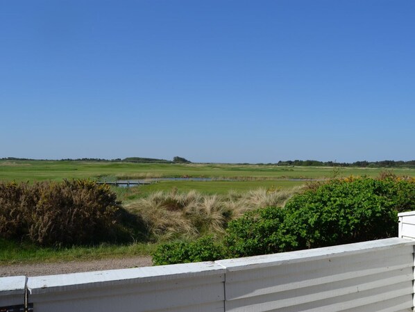 Une vue sur un terrain de golf, avec un ciel dégagé, une étendue d’eau et une clôture blanche au premier plan.