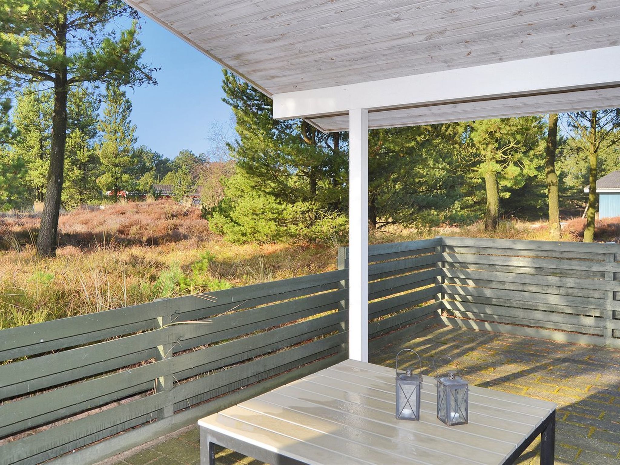 A covered outdoor seating area with a table and benches, surrounded by trees and a natural landscape.