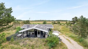 Uma casa moderna com telhado inclinado, um pátio com mobiliário de exterior e vista para o campo ao redor.