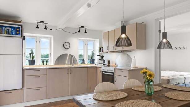 Una cocina moderna con comedor, que presenta una mesa de madera con individuales tejidos, un horno empotrado e iluminación colgante.