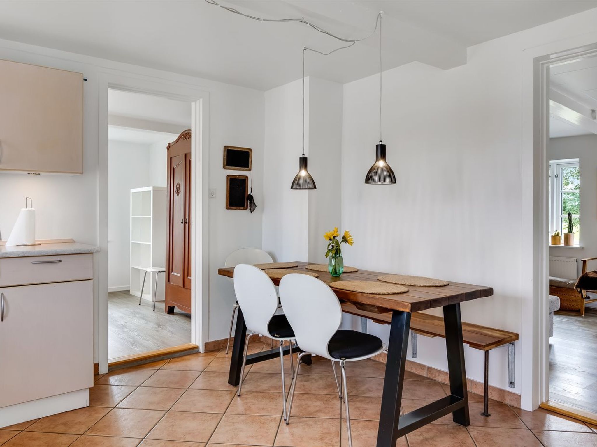 Una cucina moderna con mobili bianchi, un tavolo da pranzo in legno, due sedie bianche e lampade a sospensione.