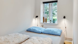 Un dormitorio con una cama, dos lámparas de noche, una ventana con vistas a la vegetación y un radiador.
