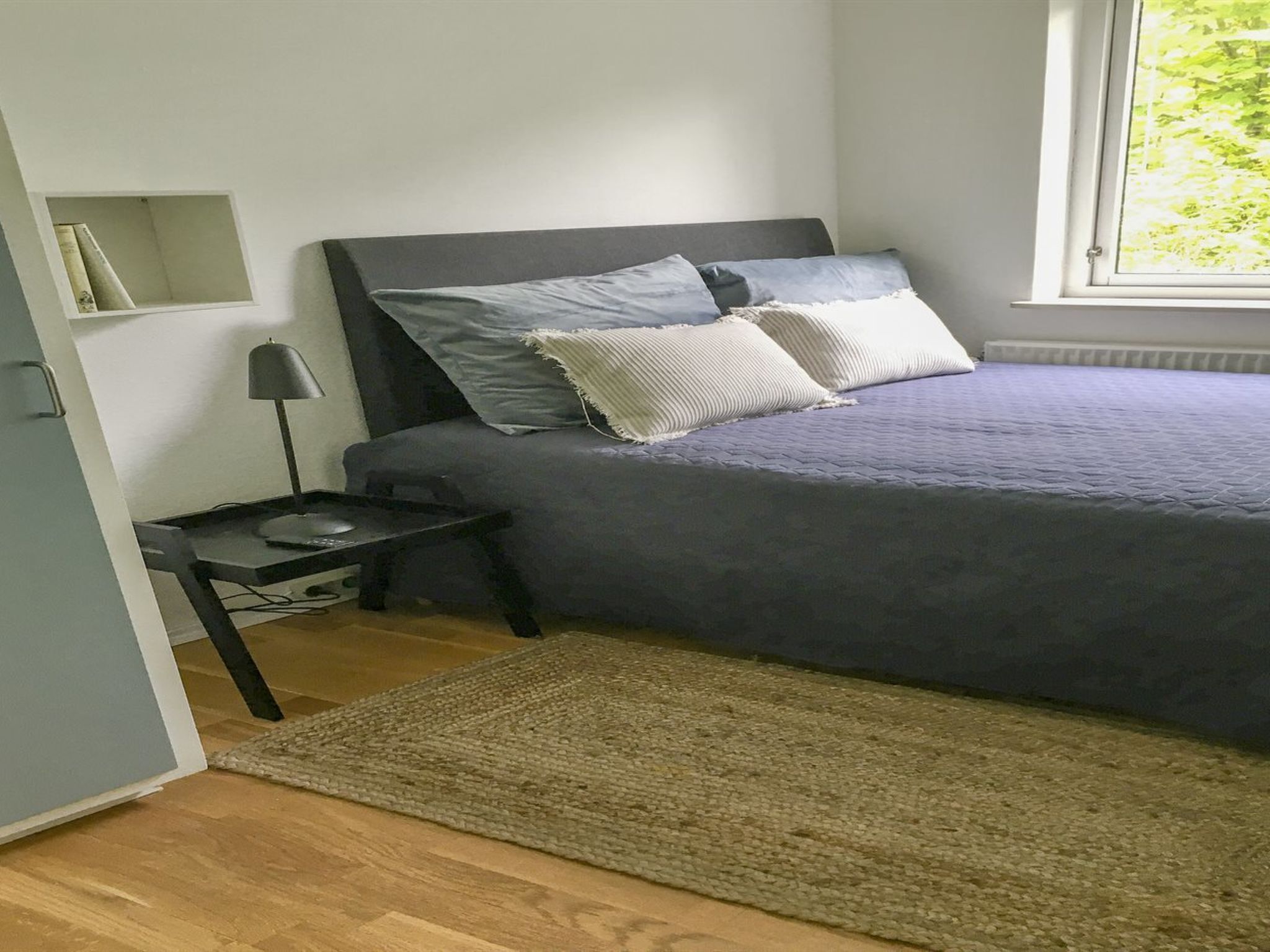Une chambre à coucher comprenant un lit, une table de chevet, une lampe et une fenêtre donnant sur un paysage verdoyant.