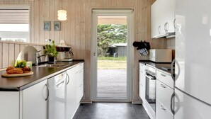 A modern kitchen with white cabinets, a stainless steel refrigerator, and a black countertop. There is a door leading to an outdoor area with a view of greenery. - "Annemia" - 200m from the sea by Interhome (Thisted)