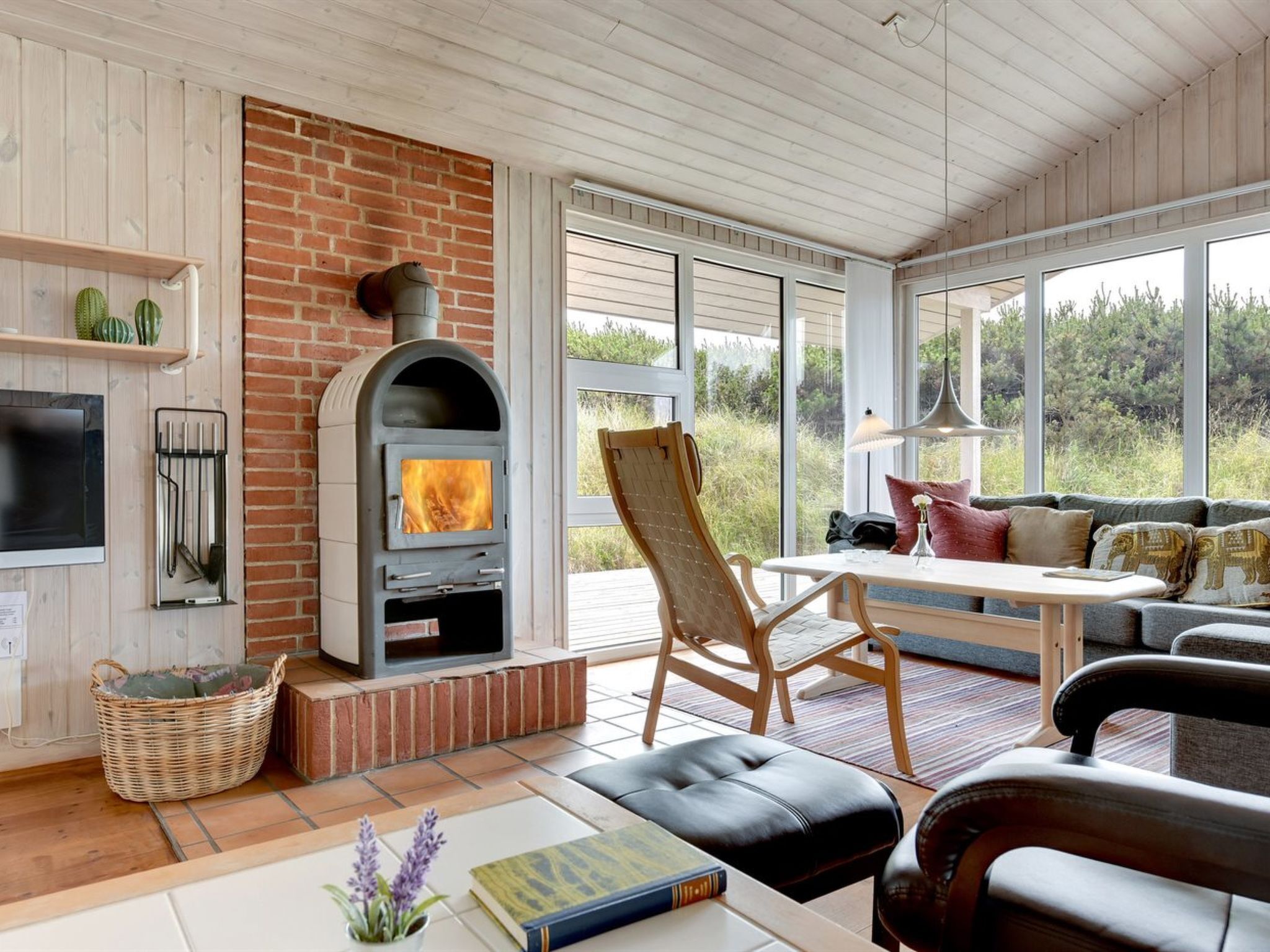 A cozy living room with a fireplace, comfortable seating, and large windows offering a view of the outdoors.