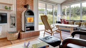 A cozy living room with a fireplace, comfortable seating, and large windows offering a view of the outdoors. - "Annemia" - 200m from the sea by Interhome (Thisted)