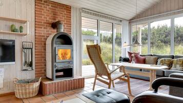 A cozy living room with a fireplace, comfortable seating, and large windows offering a view of the outdoors.