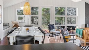 Ein Essbereich mit einem langen Tisch, Stühlen und einer hängenden Leuchte. Große Fenster bieten Ausblicke ins Freie.
