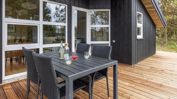 Ein moderner Essbereich im Freien mit einem dunklen Holztisch und -stühlen, großen Fenstern und einer Holzterrasse.