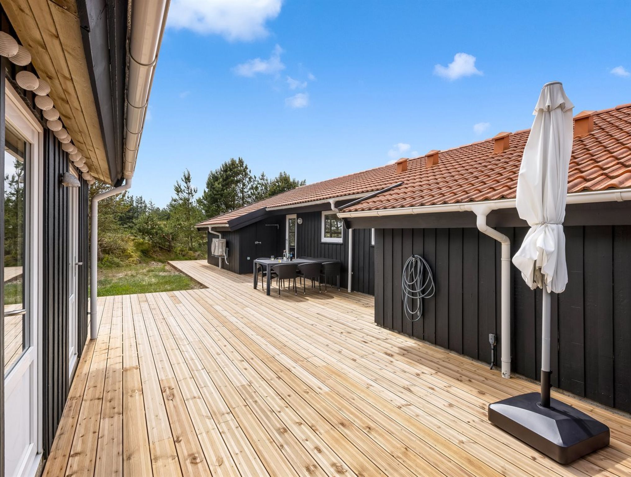 A wooden deck with a table and chairs, a covered outdoor area, and a building with a tiled roof.
