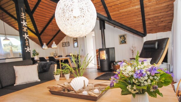 Un salon chaleureux avec une table en bois, un vase blanc orné de fleurs et un grand luminaire en fibres tressées.