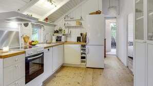 Eine moderne Küche mit weißen Schränken, Holz Arbeitsplatten und einem eingebauten Backofen. Es gibt ein Waschbecken mit Armatur, eine Mikrowelle und einen Kühlschrank. Der Boden ist aus Holz, und die Decke hat sichtbare Holzbalken.