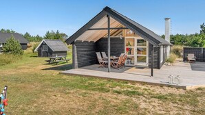 Eine moderne Holzblockhütte mit überdachter Terrasse, einem Essbereich und einem sichtbaren Schornstein.