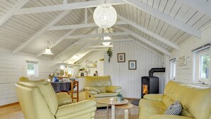 Ein großzügiges Loft mit hohen Decken, einer zentralen Sitzecke mit gelben Ledersofas, einer Küche im Hintergrund und einem Kaminofen.