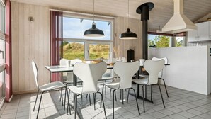 Una cocina moderna con muebles blancos, un ventanal grande y una zona de comedor con sillas blancas y una lámpara colgante negra.