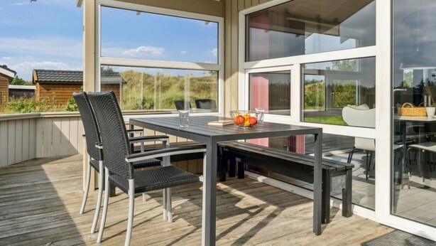 Un patio exterior con una mesa y sillas, ventanas amplias y vistas del entorno.