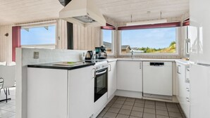 Cocina compacta con armarios blancos, encimera negra, estufa y lavavajillas. Ventanas que ofrecen luz natural y vistas al exterior.