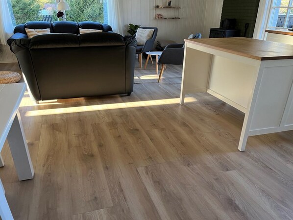 Una sala de estar moderna con un sofá de cuero oscuro, una mesa de centro de madera y una cocina con encimera blanca.
