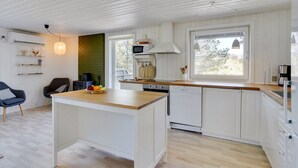 Moderni keittiö, jossa on valkoiset kaapit, puinen keittiösaareke ja suuri ikkuna, josta tulee runsaasti luonnonvaloa.