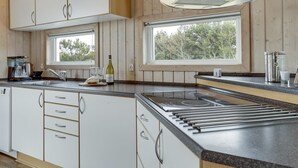 Een moderne keuken met witte kasten, een roestvrijstalen afzuigkap, een ingebouwde kookplaat en een raam met uitzicht op bomen.