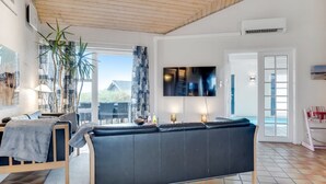 A modern living room with a black sofa, a TV, and a large window overlooking a garden. - "Palli" - 600m from the sea by Interhome (Thisted)