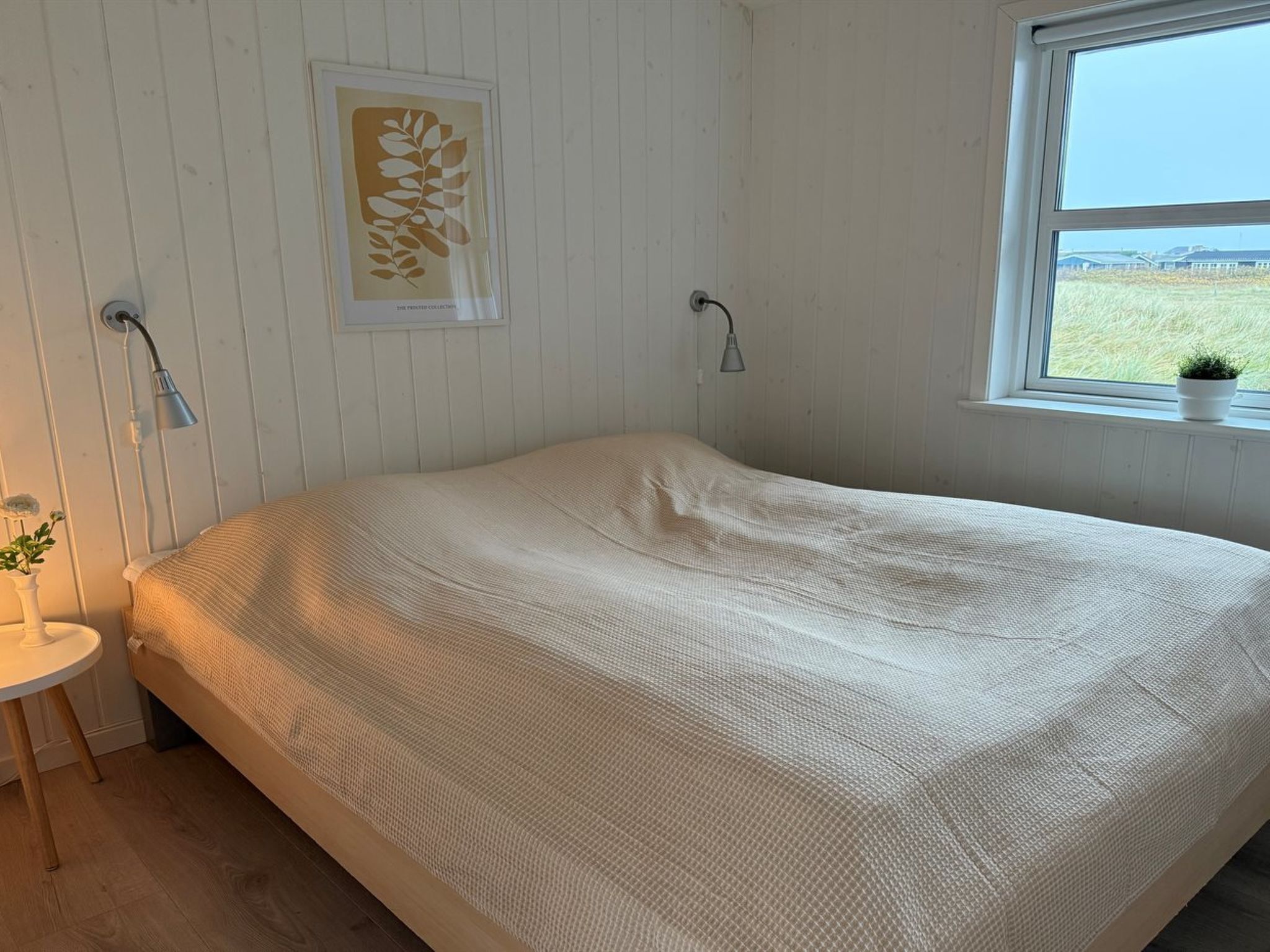 Makuuhuoneessa on sänky, yöpöytä, lamppu, ikkuna ja seinälle ripustettu taulu.