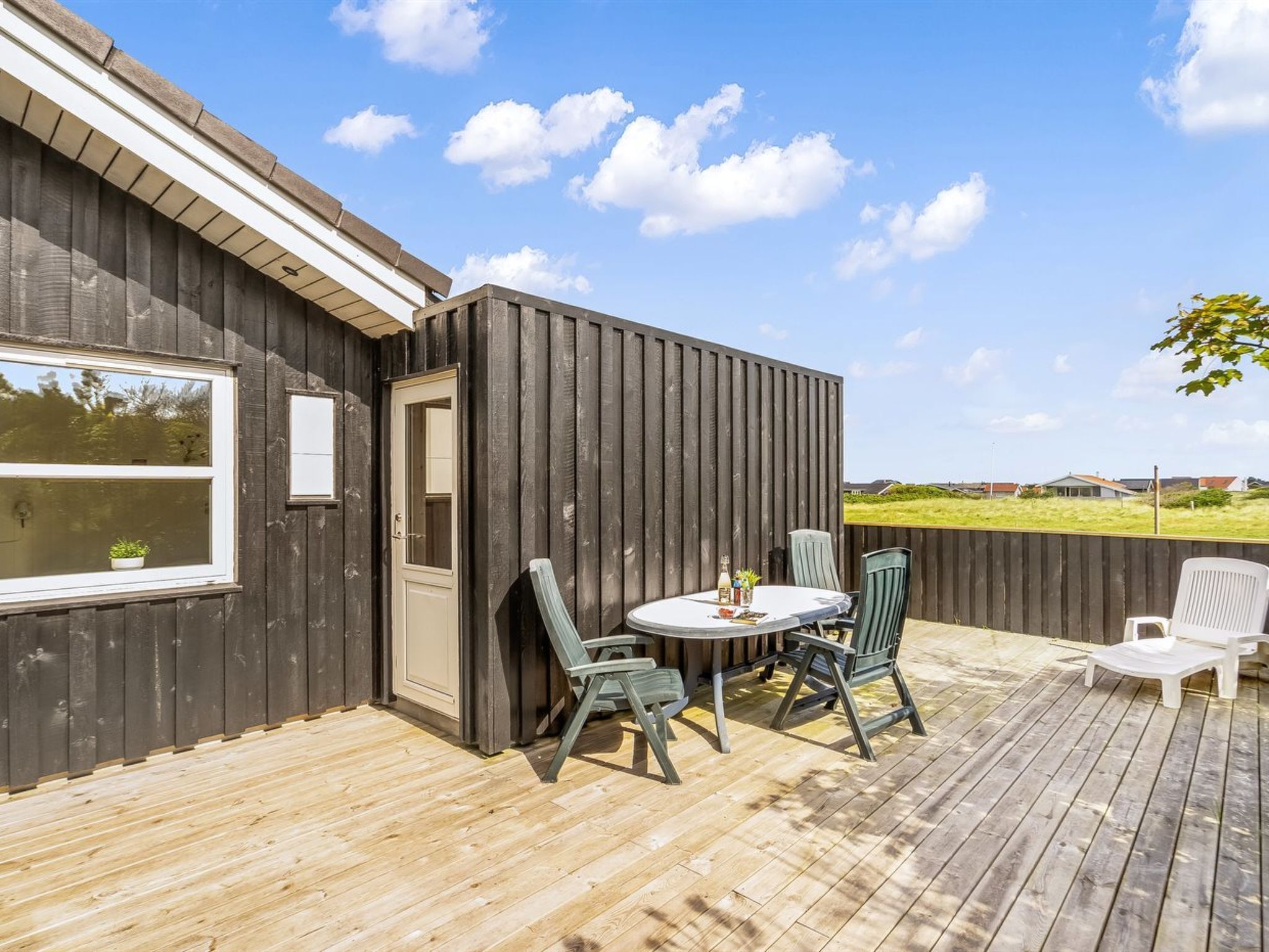 A wooden deck with a table and chairs, a door, and a window.