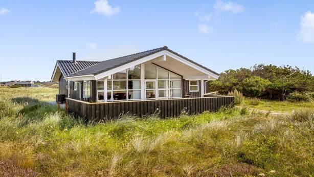 Et moderne hus med stor terrasse, omgivet af højt græs og træer.