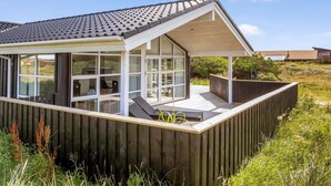 Et moderne hus med store glaspartier, træterrasse og et skråt tag.