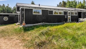 Un edificio moderno negro con el número '3' en la fachada, una ventana pequeña y un patio con mobiliario exterior.