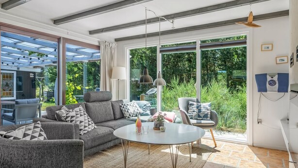 Una sala de estar moderna con sofá, sillón y mesa de centro, ventanas amplias y una pérgola.