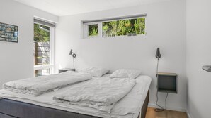 Un dormitorio moderno con una cama, dos mesitas de noche, una ventana con vistas a zonas verdes y una lámpara en el techo.
