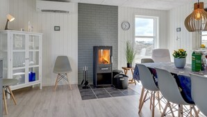 A modern kitchen with a central wood-burning stove, white cabinetry, and a dining area with a table and chairs. - "Ibo" - 900m from the sea by Interhome (Thisted)