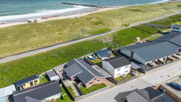 Vue aérienne d’une zone résidentielle côtière, avec des maisons, une route et une plage.