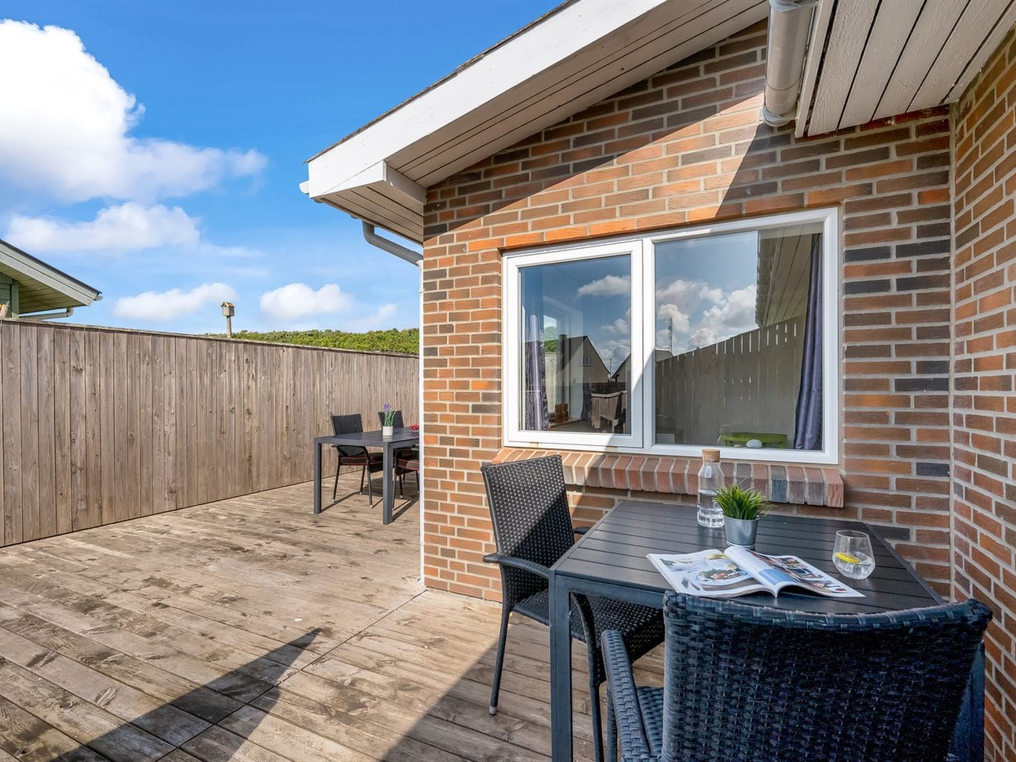 En patio med et bord og stole, en træterrasse og en murstensvæg.