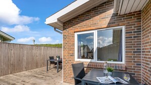 En patio med et bord og stole, en træterrasse og en murstensvæg.