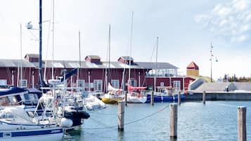 Un port de plaisance où sont amarrés plusieurs bateaux, avec des pilotis en bois et des bâtiments aux façades rouges et jaunes.