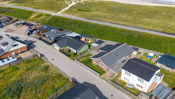 Oversigtsbillede af et kystnære boligområde med huse, en strand og en moler.